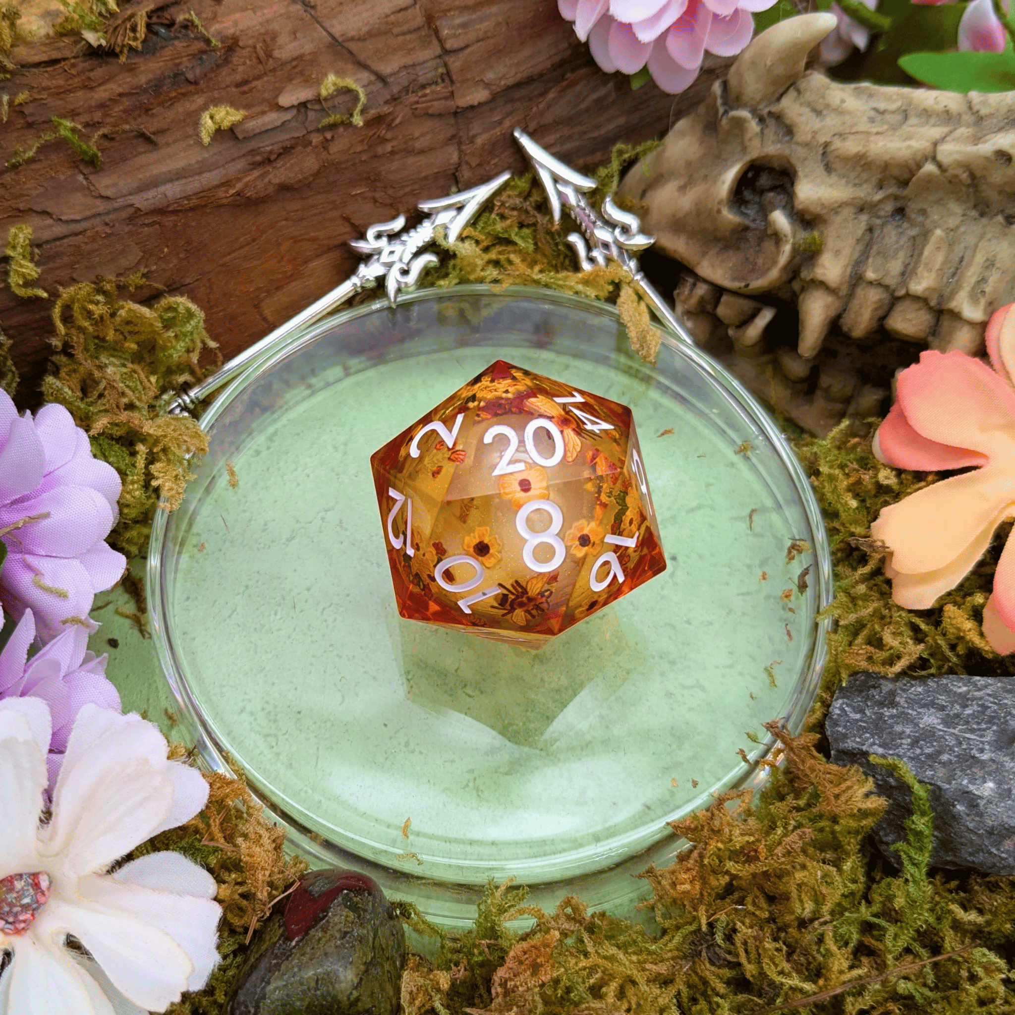 Translucent orange polyhedral dice with numbers on a green surface surrounded by flowers and bones.
