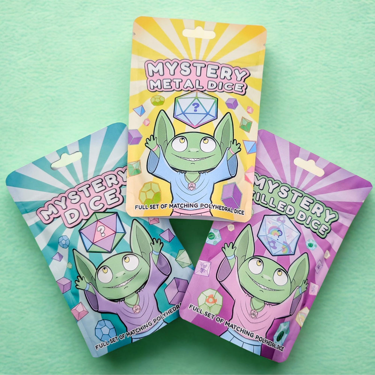 Three hanging Mystery Dice bundle packages, each featuring a green goblin character and text identifying them as Mystery Metal Dice, Mystery Dice, or Mystery Filled TTRPG dice.